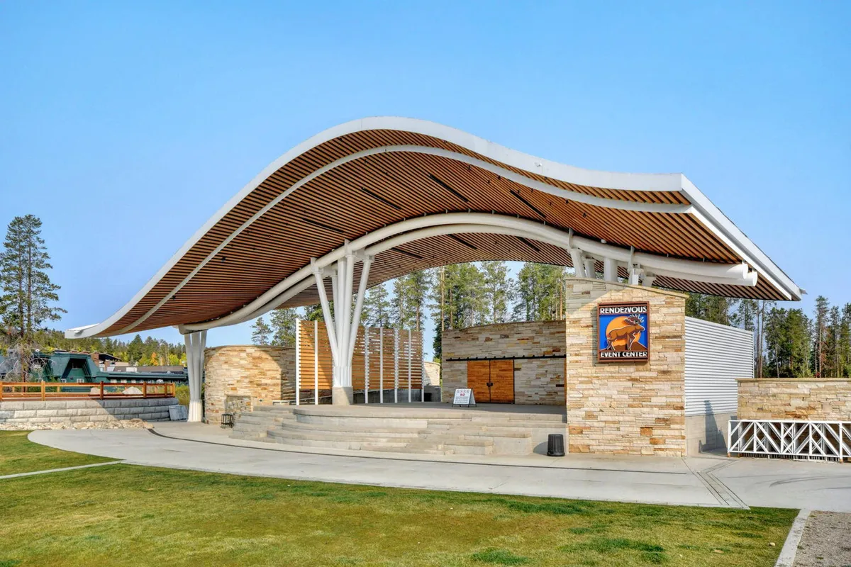 An outdoor scene highlighting the distinctive curved roof and stone facade of the Hideaway Park amphitheater, surrounded by open space for gatherings. The stage area is ready for performances and festivals, capturing the community’s hub for year-round events.