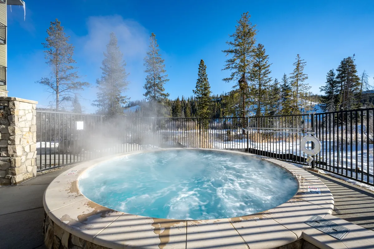 An outdoor hot tub surrounded by pine trees and mountains. The tranquil scene invites relaxation, with the warm water contrasting against the cool mountain air. Guests can socialize or enjoy solitude while being immersed in nature.