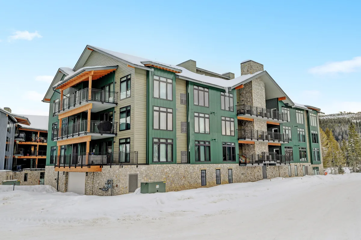 An exterior view of the property with a green and stone facade, wooden balconies, and a snowy setting. The inviting balconies overlook a winter wonderland, suggesting easy access to both relaxation and adventure.