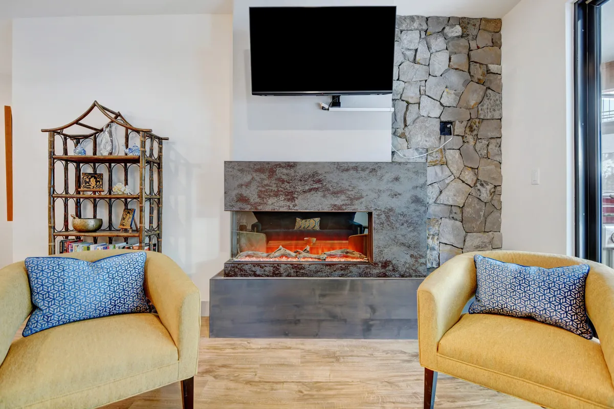 A warmly lit living area featuring a modern fireplace as its centerpiece, surrounded by comfortable seating and a decorative shelf. The atmosphere is intimate and inviting, suggesting a perfect spot for couples to unwind after a day exploring Winter Park, with opportunities for cozy fireside relaxation.