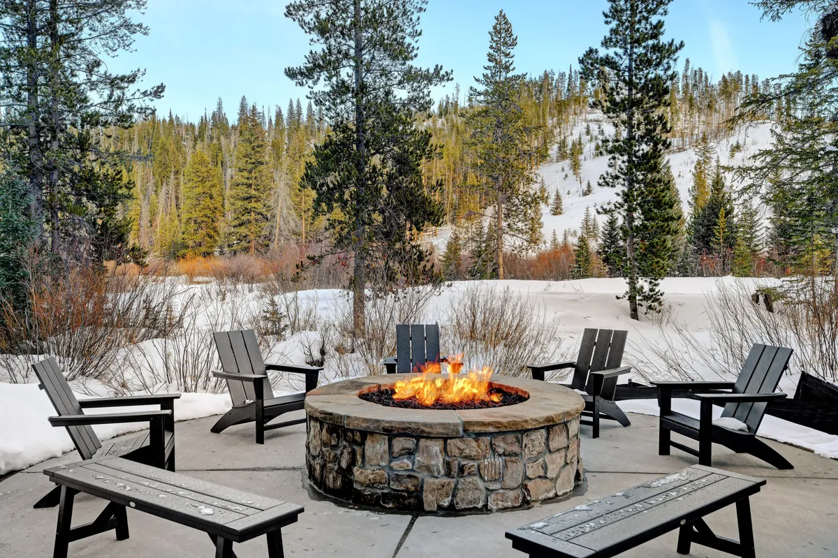 A circular fire pit with comfortable seating encircled by snow, with pine trees and mountains in the distance. The warm glow from the fire creates an inviting setting for gatherings, storytelling, and stargazing on chilly evenings.