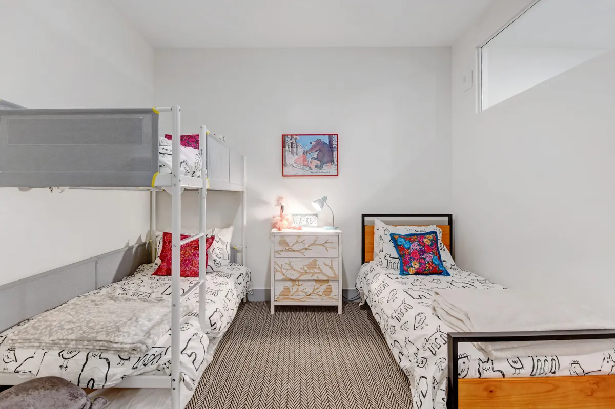 A playful bunk room with a bunk bed, an additional twin bed, a nightstand, and cheerful wall art. The space is designed for both fun and function, accommodating children or friends with flexibility and comfort.