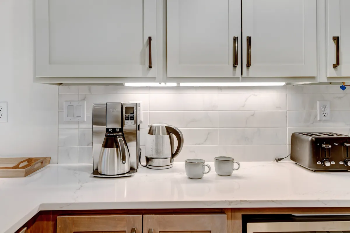 A stylish kitchen countertop with a coffee maker, toaster, kettle, mugs, and other breakfast essentials arranged neatly. The setting suggests a cozy, personalized morning ritual, possibly enjoyed while appreciating mountain views from a private patio.